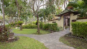 A stone pathway leading to a traditional-style building with a tiled roof, surrounded by lush greenery and various plants.