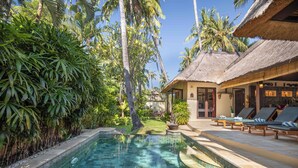 A pool area with lounge chairs, a thatched-roof building, and lush tropical vegetation. - Alam Anda Ocean Front Resort & Spa (Tejakula)