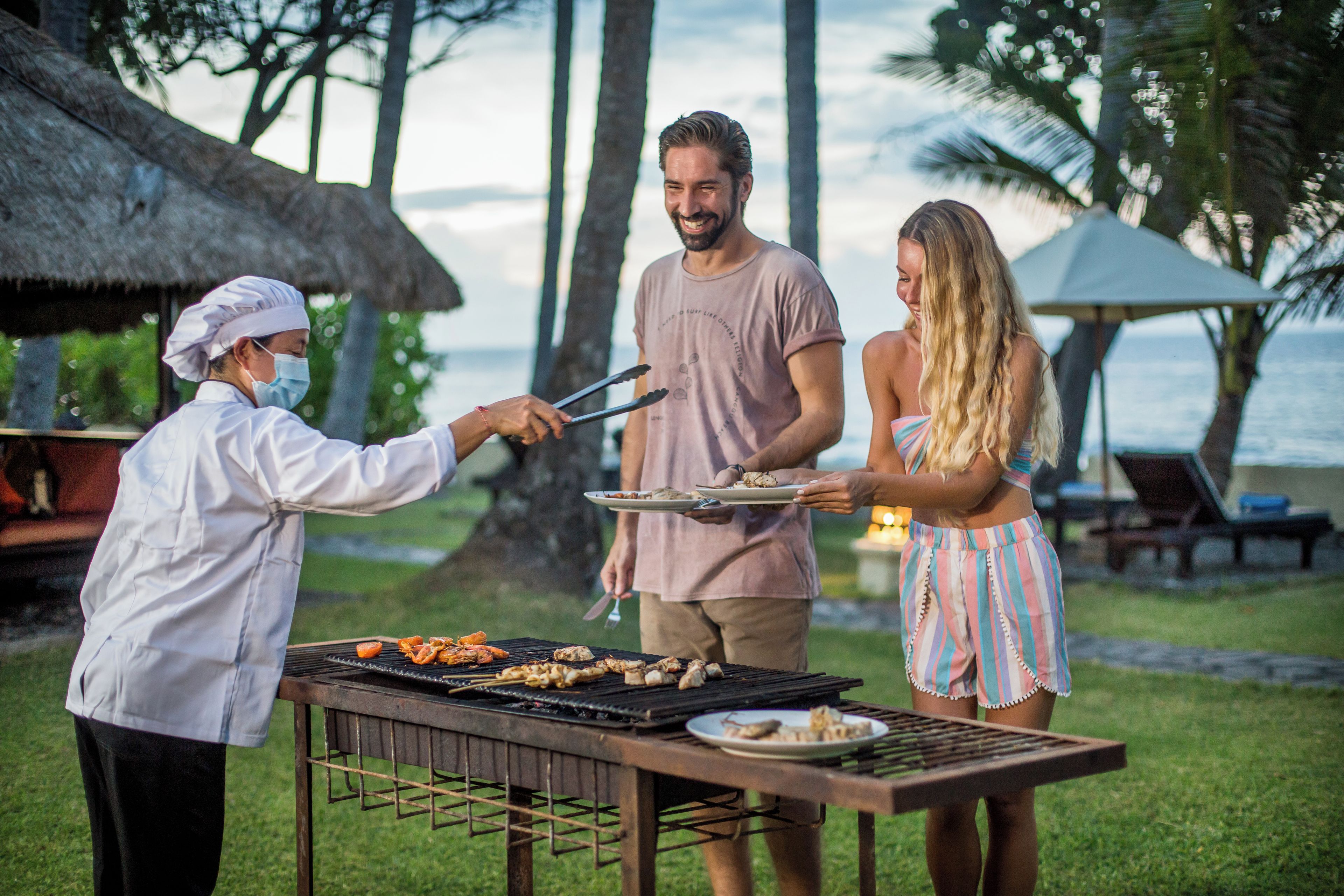 A person grilling food outdoors with a table and chairs nearby.