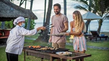 A person grilling food outdoors with a table and chairs nearby.