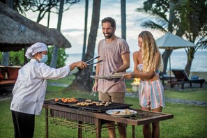 A person grilling food outdoors with a table and chairs nearby. - Alam Anda Ocean Front Resort & Spa (Tejakula)