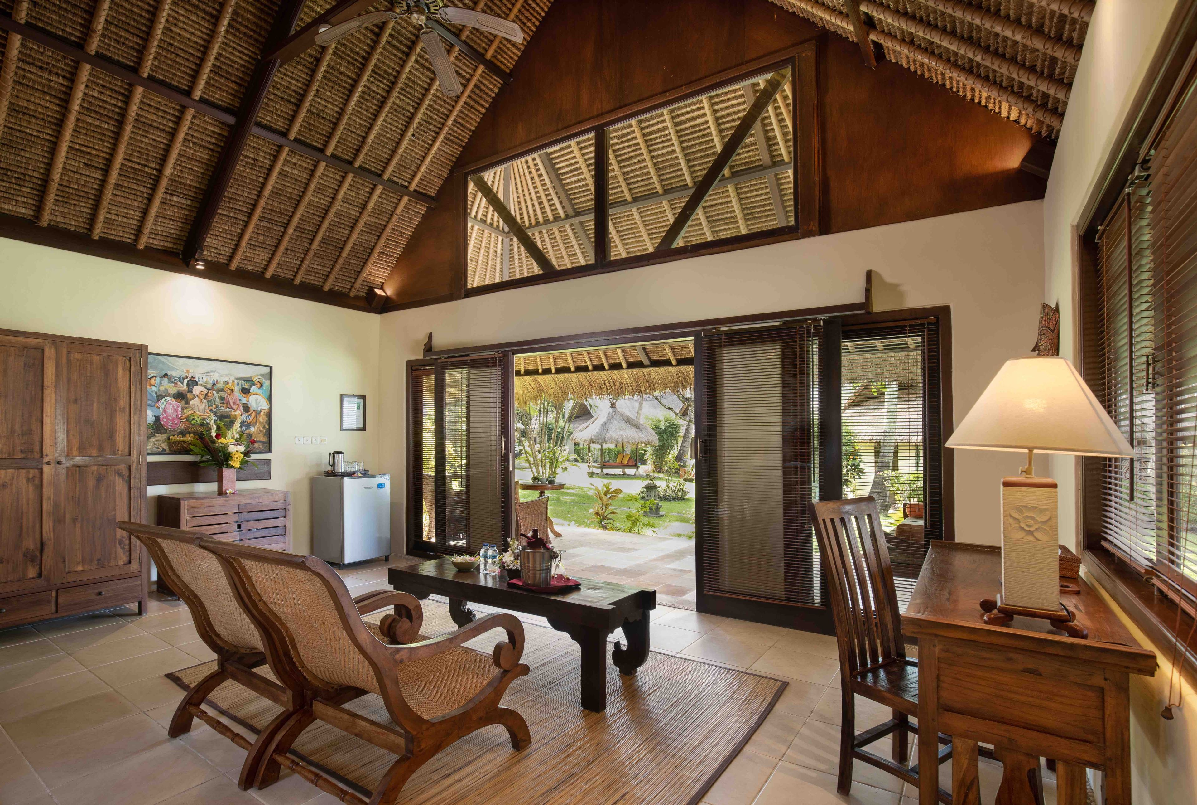 Um quarto amplo com teto alto, mobiliário de madeira, uma mesa de jantar e vista para um jardim através de amplas portas de correr.