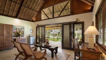 Um quarto amplo com teto alto, mobiliário de madeira, uma mesa de jantar e vista para um jardim através de amplas portas de correr.