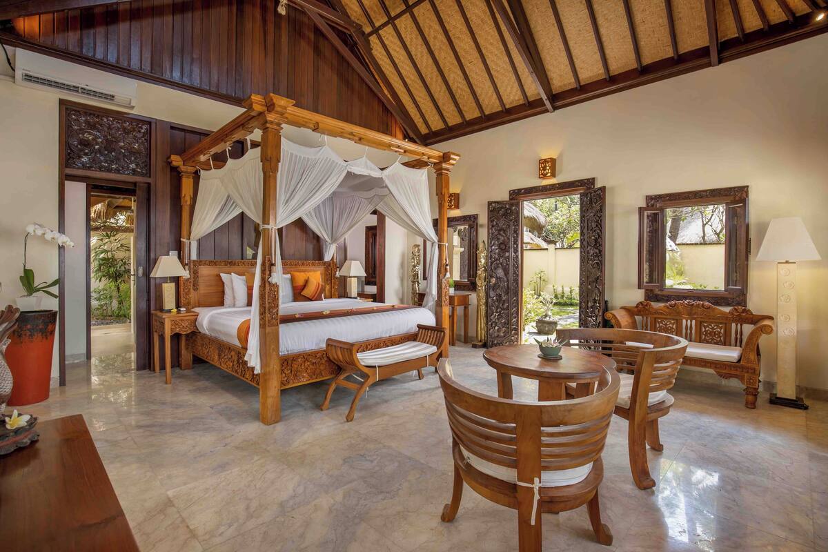 A spacious bedroom with a four-poster bed, a wooden dining table with chairs, and a sitting area with a bench.