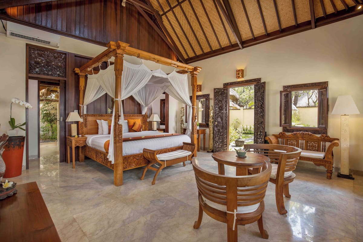 A spacious bedroom with a four-poster bed, a wooden dining table with chairs, and a sitting bench.