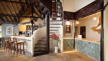 A bar area with a stone counter, wooden chairs, and a staircase with a decorative railing.