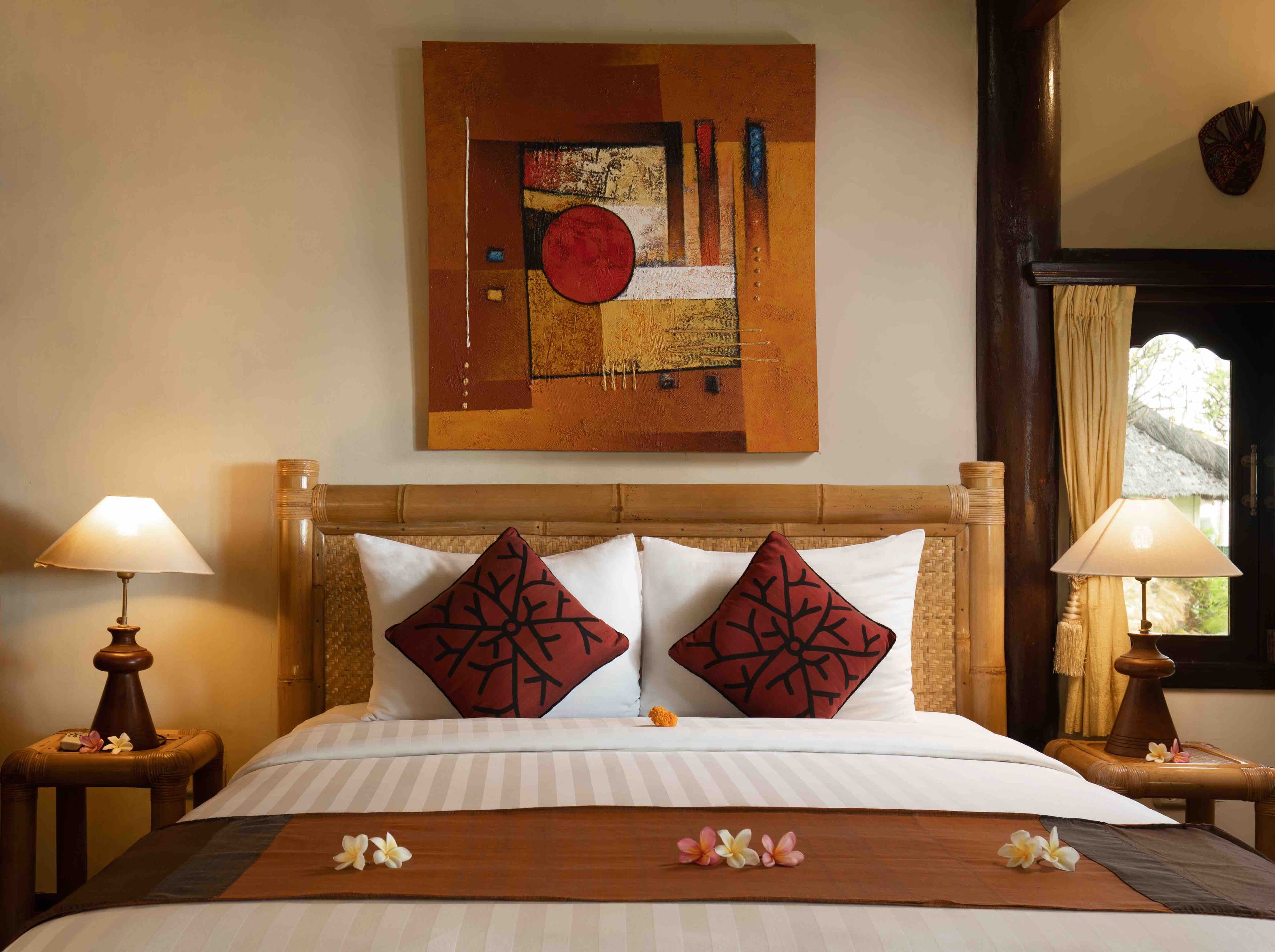 A neatly made bed with white bedding and two red decorative pillows, a wooden headboard, and a wall-mounted abstract painting.