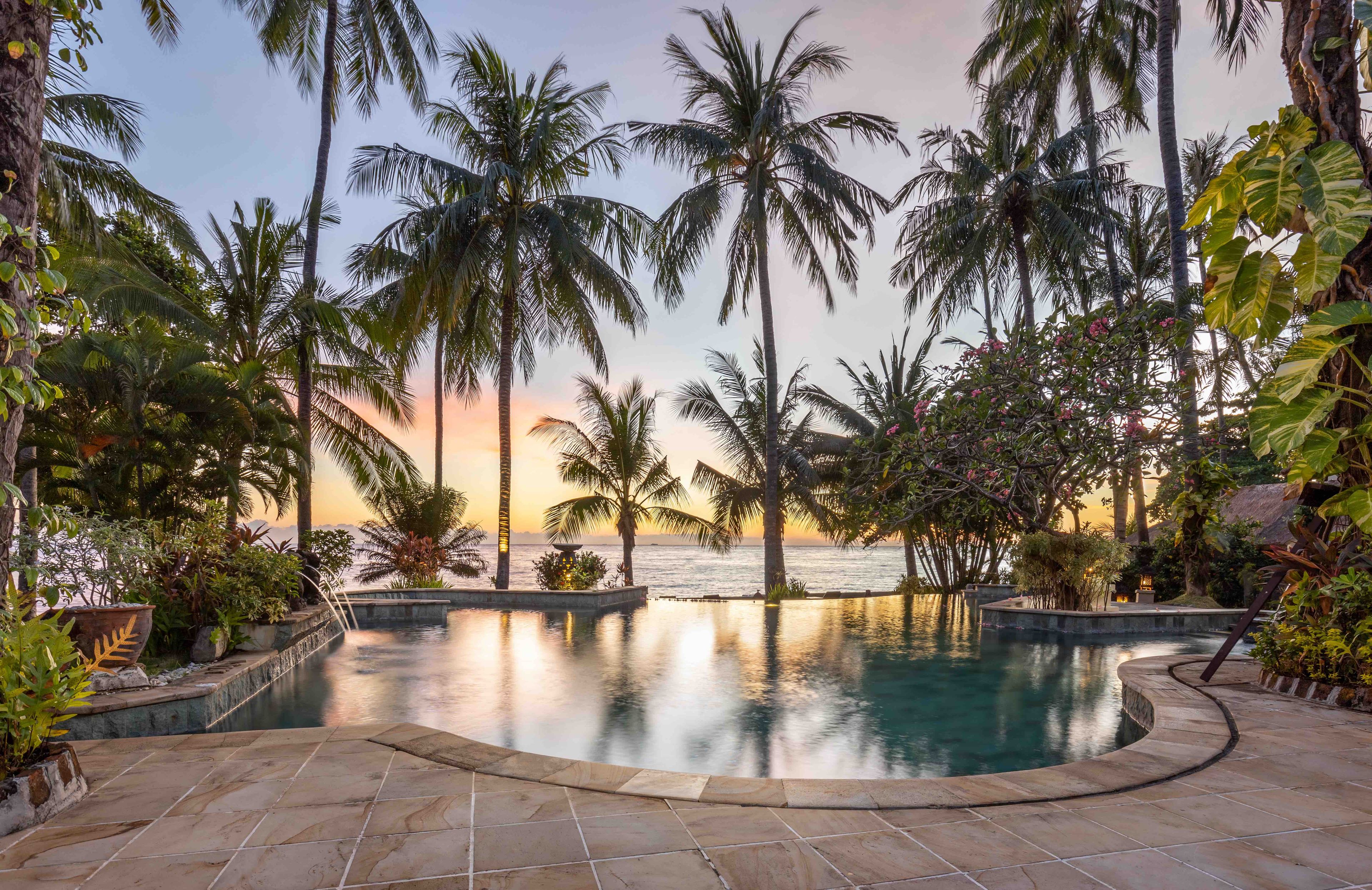 Una piscina rodeada de palmeras y vista al atardecer.