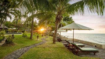 Cenário de resort tropical com um caminho que leva a espreguiçadeiras e guarda-sóis na beira da praia, com vista para o oceano.