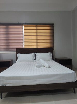 A neatly made bed with white linens, two bedside tables, and a window with blinds. - OYO 881 Nest Suites (Quezon City)