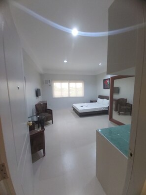 Une chambre avec un lit, un bureau et une chaise. Il y a une fenêtre avec des stores, une porte et un miroir au mur.