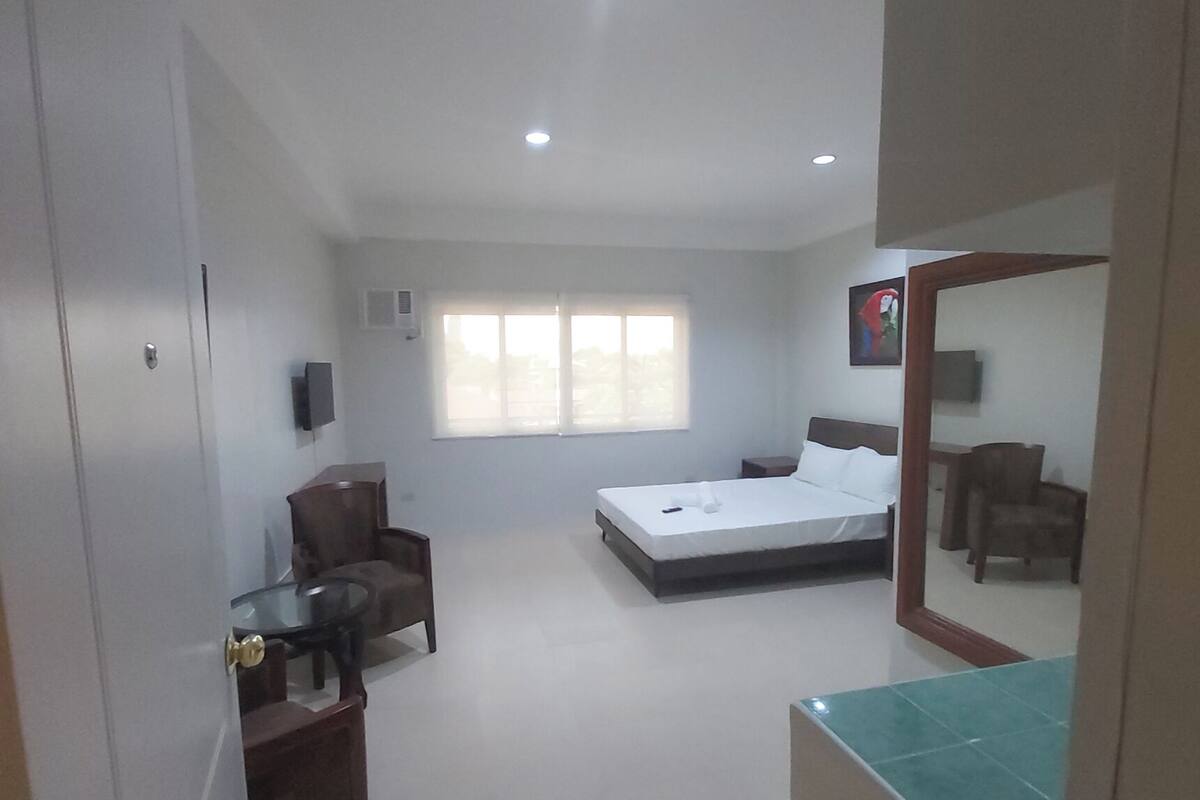 Un dormitorio con cama, escritorio y silla. Hay una ventana con persianas, una puerta y un espejo en la pared.