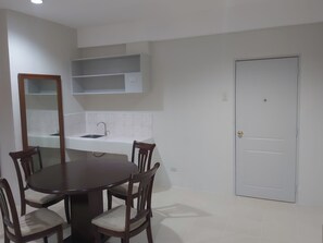 A dining area with a round table and four chairs, a kitchen with a sink and cabinets, and a white door. - OYO 881 Nest Suites (Quezon City)