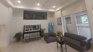 A spacious lobby with a grey sofa, a small table with a vase of flowers, a seating area with chairs, a large framed artwork on the wall, and a calendar. - OYO 881 Nest Suites (Quezon City)