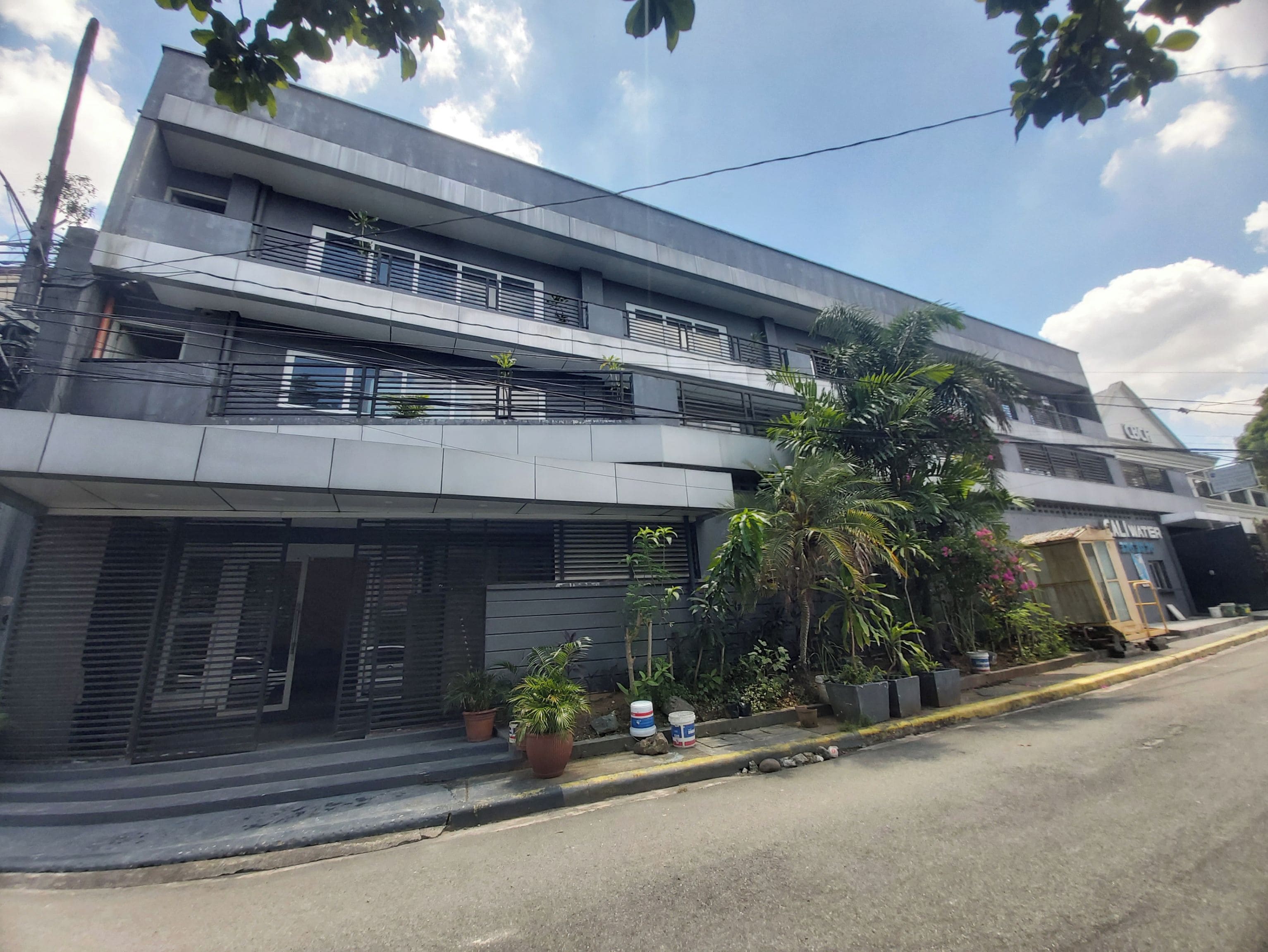 A modern two-story building with balconies, potted plants, and a visible entrance.