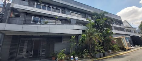 Un edificio moderno de dos pisos con balcones, plantas en macetas y una entrada visible.