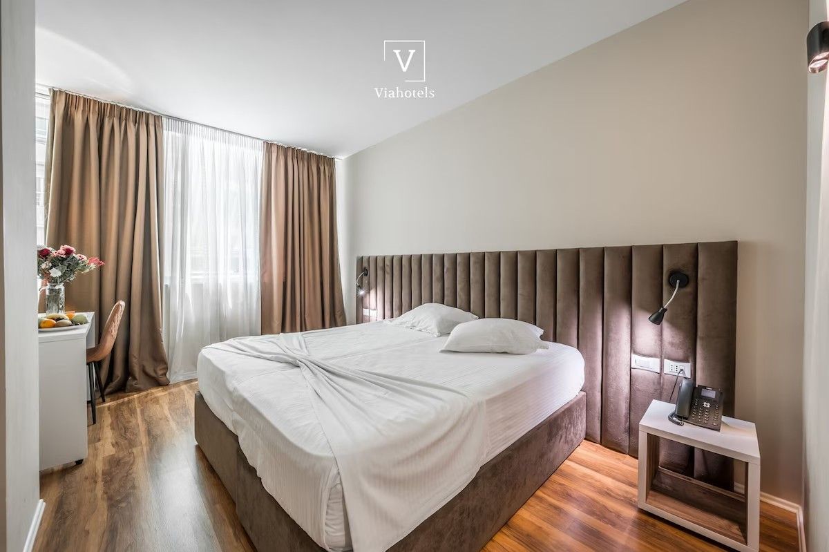 A modern hotel room with a large bed, a bedside table with a phone, and a desk with a chair.