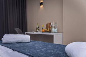 Une chambre d’hôtel avec un lit, une table de chevet sur laquelle se trouve une bouteille de champagne, un verre, une assiette de fruits et une bouteille d’eau.
