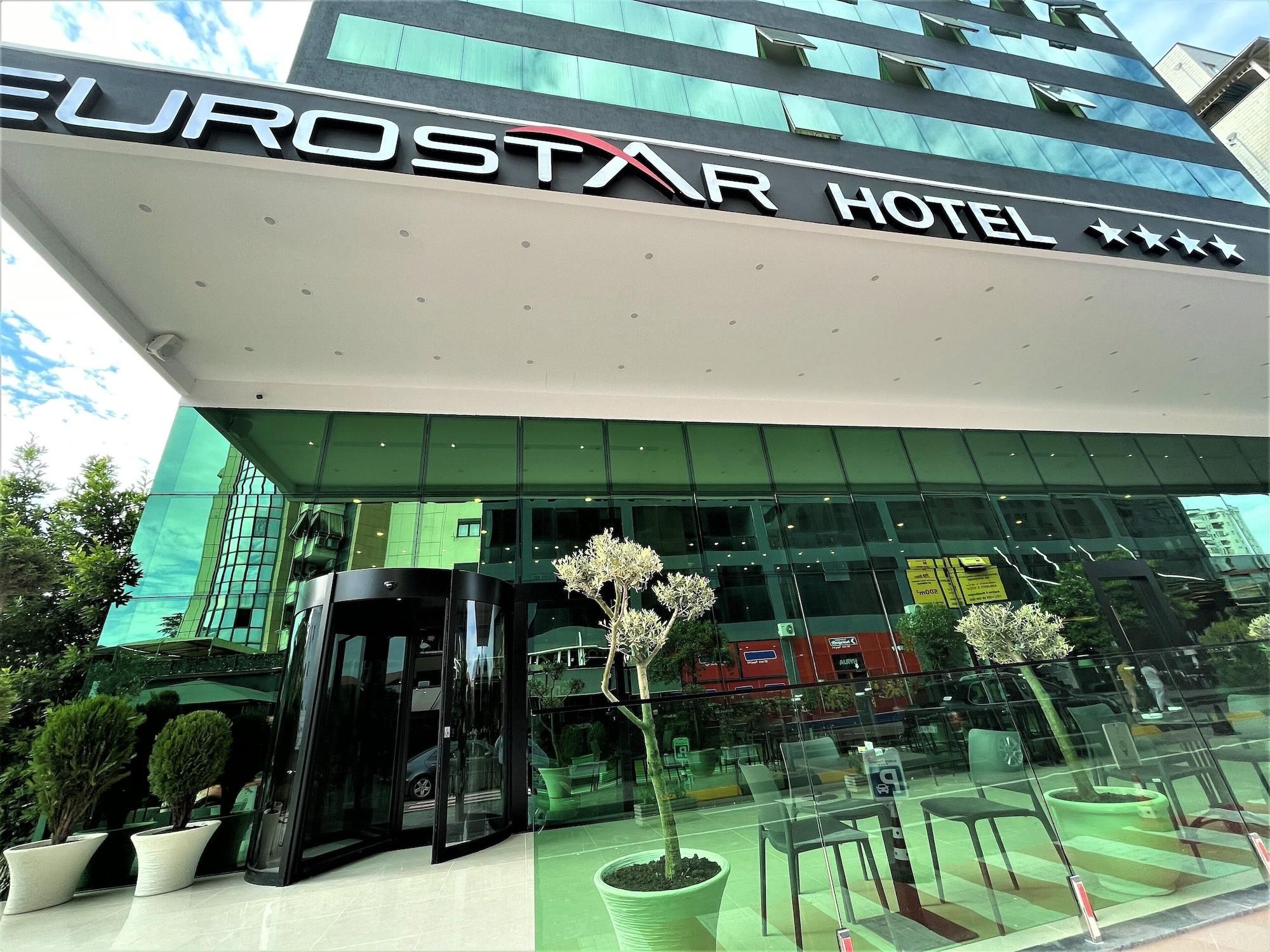 De ingang van het Eurostar Hotel met een glazen gevel, een draaideur en plantenbakken op de voorgrond.
