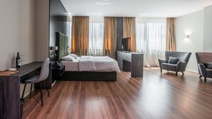 Ein modernes Hotelzimmer mit Bett, Schreibtisch, Sessel und Fernseher.