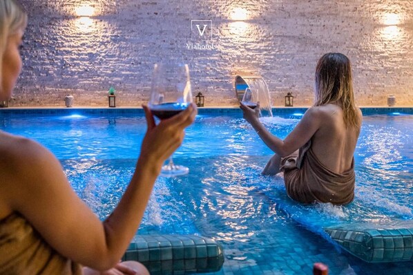 A pool area with stone walls and a person sitting in the water holding a glass. - Vh Eurostar Tirana Hotel Congress & Spa (Tirana)