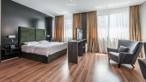 Ein modernes Hotelzimmer mit einem großen Bett, einem Schreibtisch, einem Sessel und einem Fernseher.