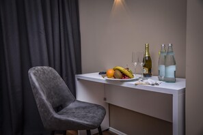 Une pièce moderne avec un fauteuil en cuir gris, un bureau blanc et une assiette de fruits et de boissons.
