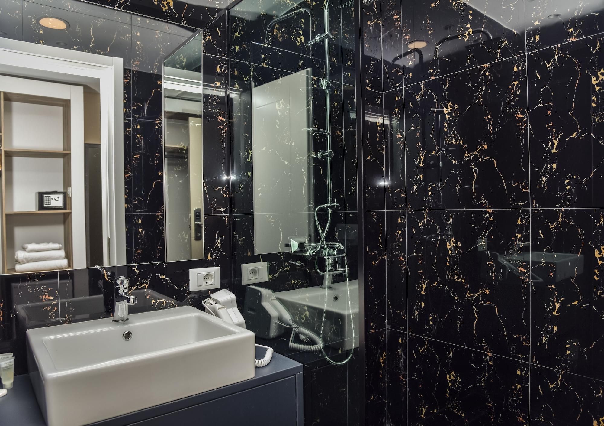 Un bagno moderno con una parete in marmo nero, un lavabo bianco, uno specchio e un soffione doccia a mano.