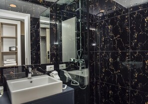 Une salle de bain moderne avec un mur en marbre noir, un lavabo blanc, un miroir et une douchette à main.