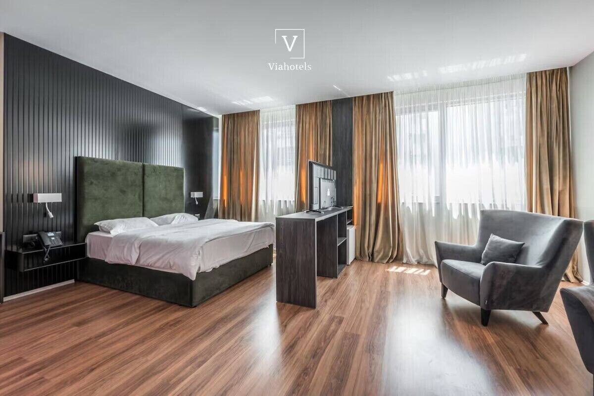 A modern hotel room with a large bed, a desk, a chair, and a TV.