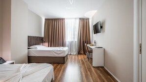 Ein Hotelzimmer mit Bett, Schreibtisch, Sessel, an der Wand befestigtem Fernseher und einem Fenster mit Vorhängen.