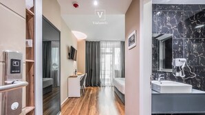 Ein modernes Hotelzimmer mit Holzboden, einem Bett, einem Schreibtisch, einem Fernseher und einem Badezimmer mit Waschbecken aus Marmor.