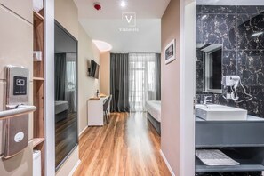 A modern hotel room with a wooden floor, a bed, a desk, a TV, and a bathroom with a marble sink. - Vh Eurostar Tirana Hotel Congress & Spa (Tirana)