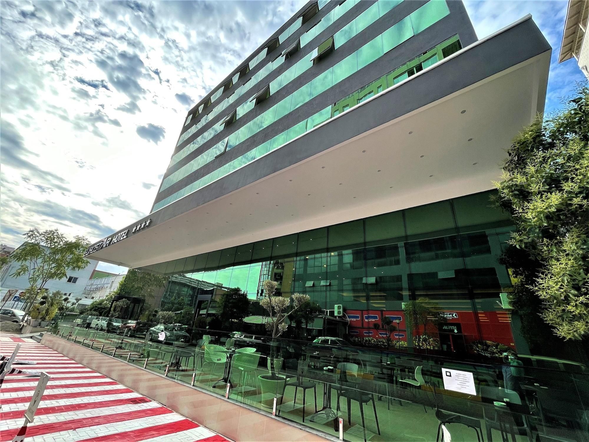 Un hotel moderno con facciata in vetro, area salotto esterna e vista aperta sul cielo.