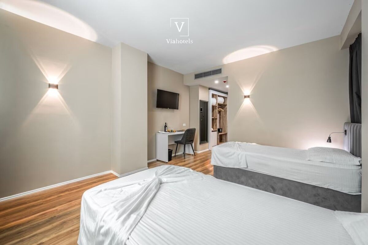 A modern hotel room with two beds, a desk, and a TV.