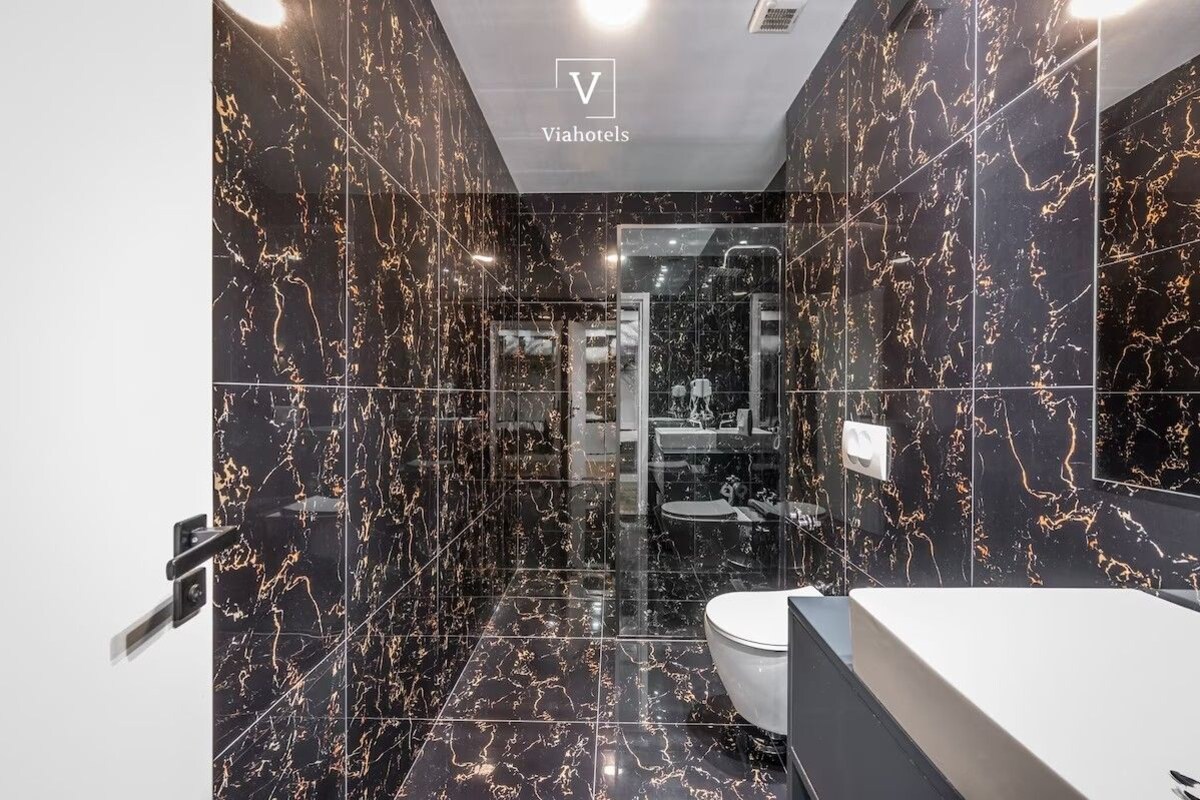 A modern bathroom with a black marble design, a glass shower enclosure, and a white sink.