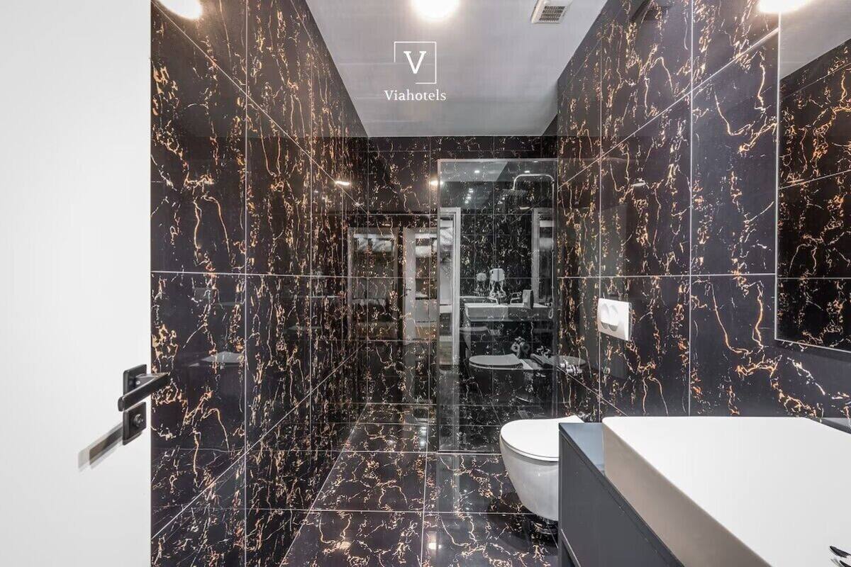 A modern bathroom with a black marble design, a glass shower enclosure, and a white sink.