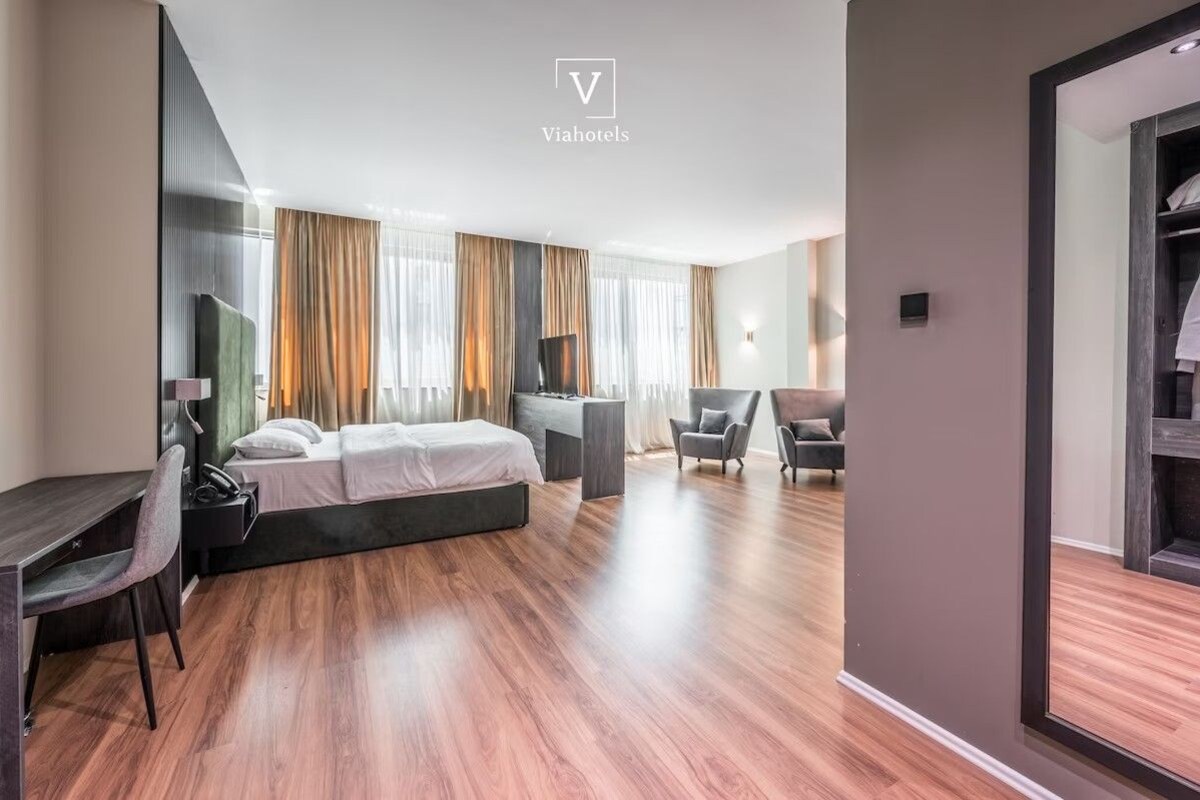 A modern hotel room with a bed, desk, chairs, and a wardrobe.