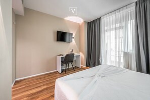 Hotellihuone, jossa on sänky, työpöytä, tuoli, seinälle asennettu televisio ja ikkuna, jossa on verhot.