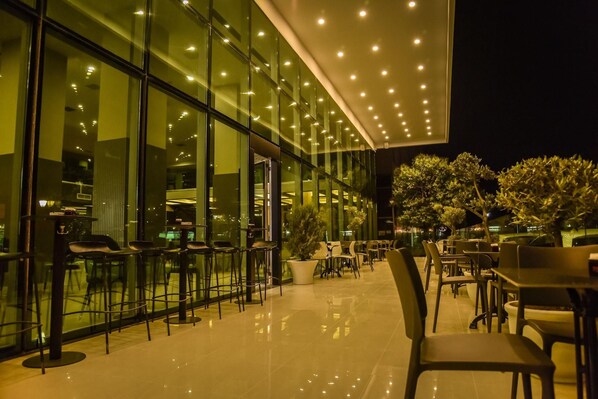 An outdoor seating area with tables and chairs, a glass building facade, and potted plants. - Vh Eurostar Tirana Hotel Congress & Spa (Tirana)