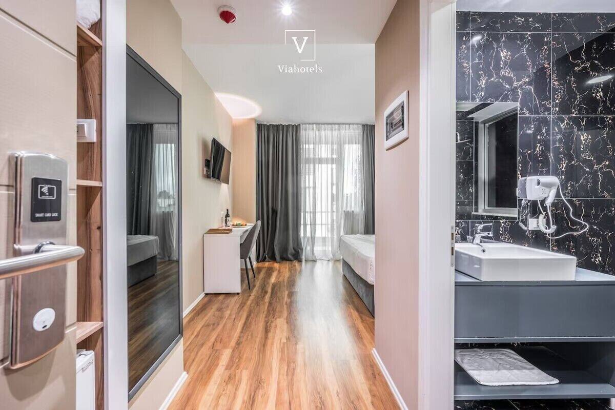 A modern hotel room with a wooden floor, a bed, a desk, a TV, and a bathroom with a marble sink.