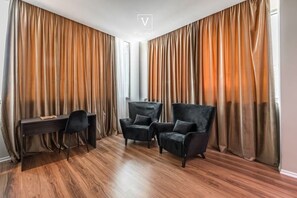 Une pièce avec un bureau, deux chaises et de grandes rideaux.