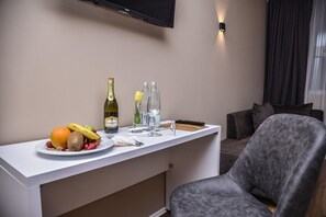 A hotel room with a white minibar, a flat-screen TV mounted on the wall, a grey upholstered armchair, and a window with dark curtains. - Vh Eurostar Tirana Hotel Congress & Spa (Tirana)