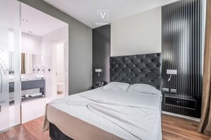 Ein modernes Hotelzimmer mit einem großen Bett, einem dunklen Kopfteil und einem begehbaren Kleiderschrank.