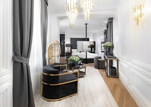 Un hall d’hôtel moderne avec un canapé noir recouvert de tissu, un fauteuil à la structure dorée et un lustre.