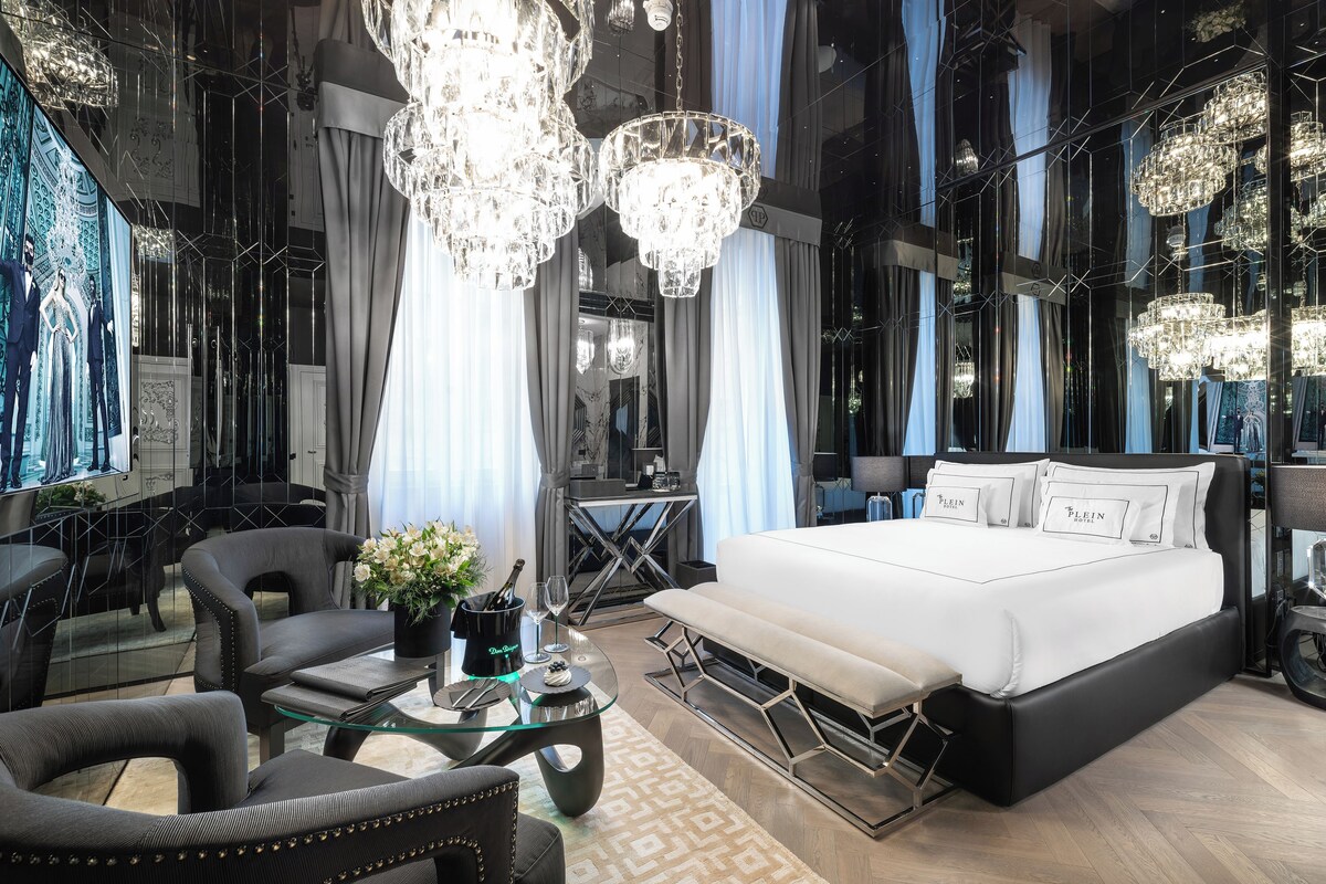 Ein modernes Hotelzimmer mit einem großen Bett, einem Glastisch und einer Sitzecke mit Sesseln.