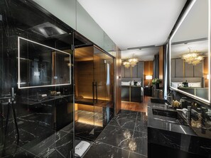 A modern hotel bathroom with a large mirror, black marble tiles, and a glass-enclosed shower area. - The Plein Hotel (Milan)