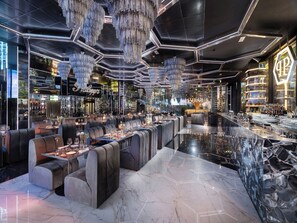 A modern bar area with seating and a bar counter, featuring geometric ceiling designs and hanging crystal chandeliers. - The Plein Hotel (Milan)