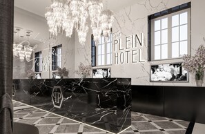 A reception area with a marble counter, chandeliers, and large windows. - The Plein Hotel (Milan)