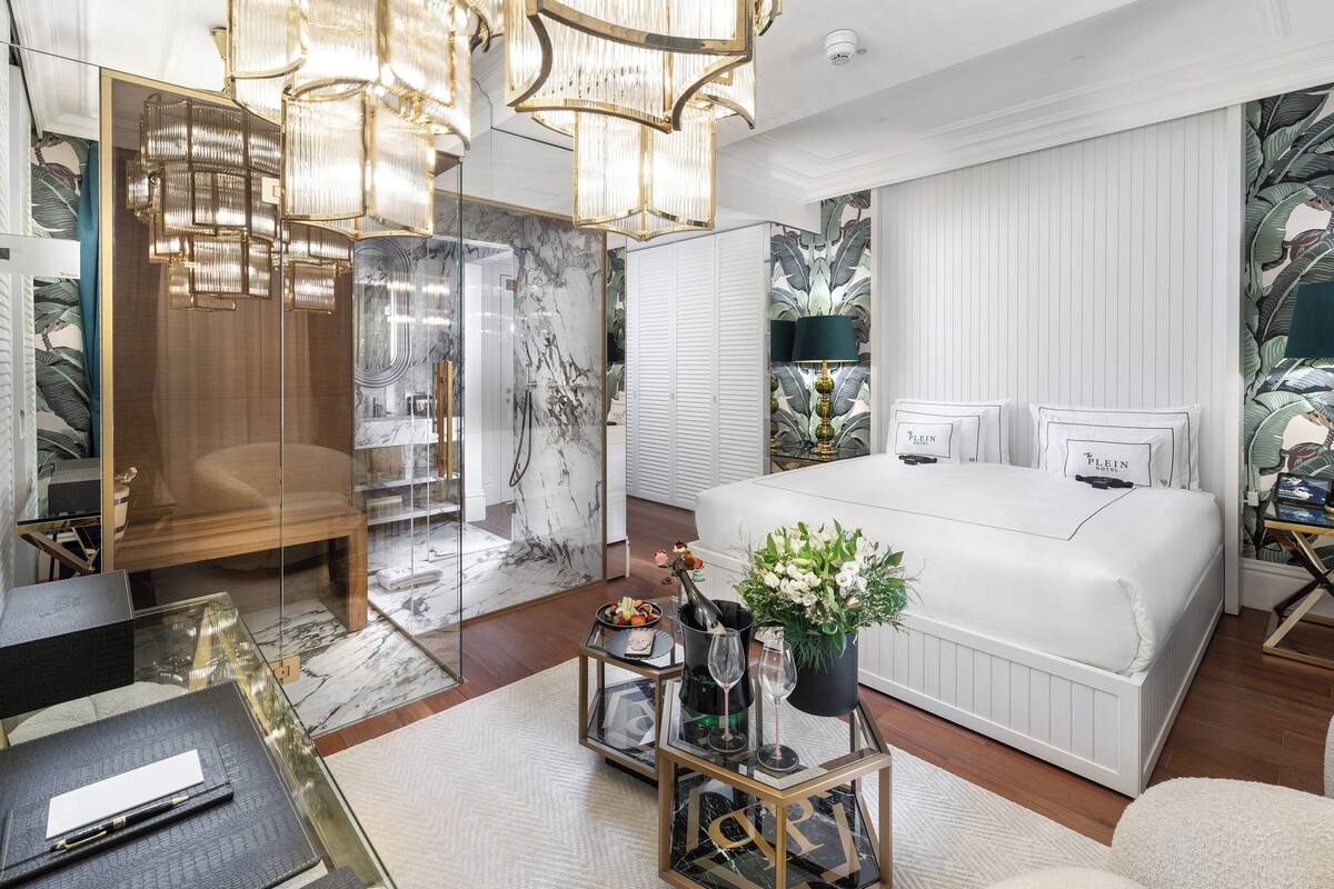 A modern bedroom with a large bed, a glass-enclosed shower, and a chandelier.